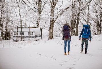 Two people walk through the snow in the woods towards their RV.