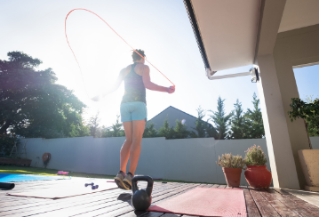 A woman jumps rope outside on her deck on a sunny day.
