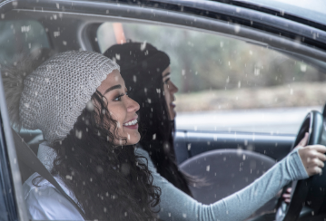 Two smiling ladies sitting in a car driving through light snow.